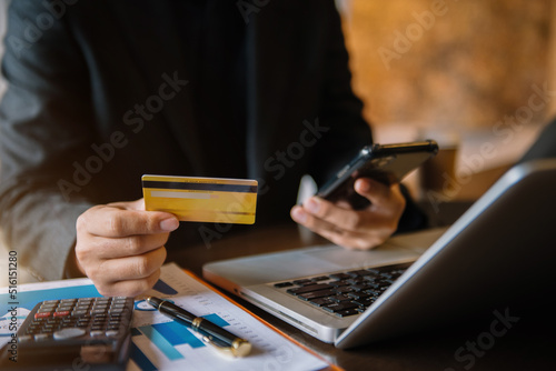 Hands holding credit card and using smartphone and laptop in office home. Online shopping.