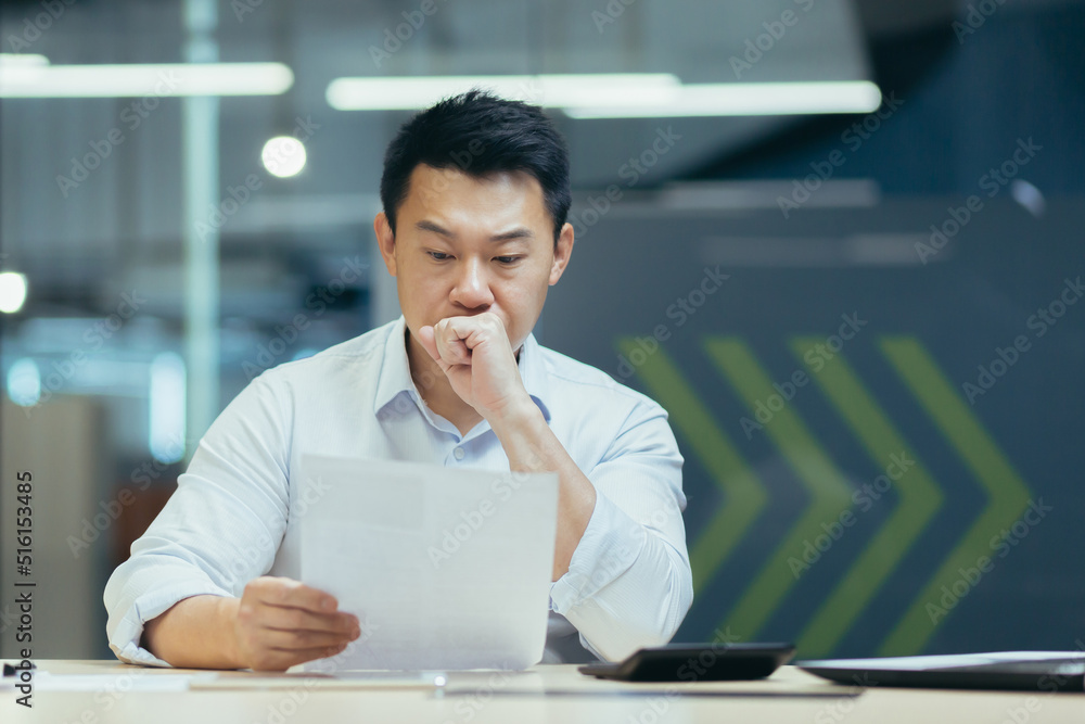 Thinking Asian businessman working in office on documents, man thinking and reading letter from bank Thinking Asian businessman working in office on documents, man thinking and reading letter from bank
