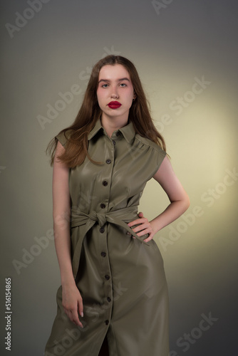 A full-length portrait of a young attractive girl with expressive red lips and long flowing smooth hair of a light shade in a stylish green dress and black shoes. Green background
