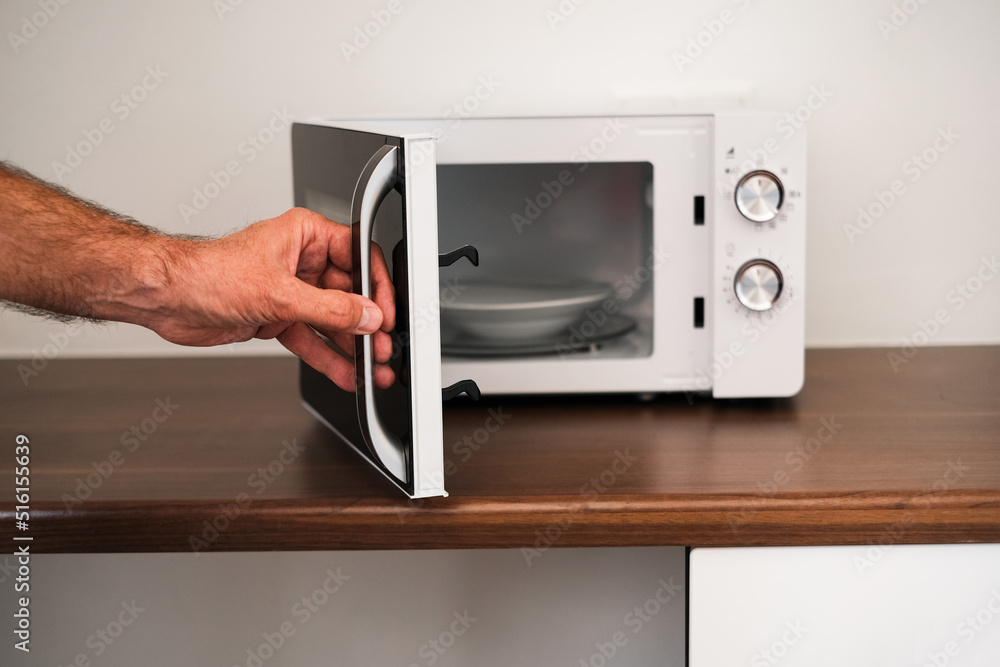Fototapeta premium a man puts a plate in the microwave to warm up his food