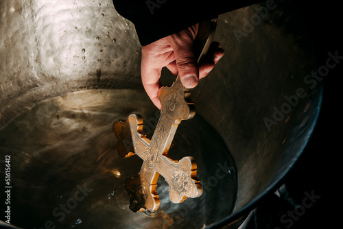A Bulgarian priest is holding a cross over water for an orthodox baby baptism. High quality photo
