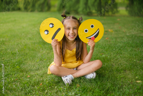 Obraz na plátně A laughing, cheerful child holds two emoticons in his hands - a sad, upset one a