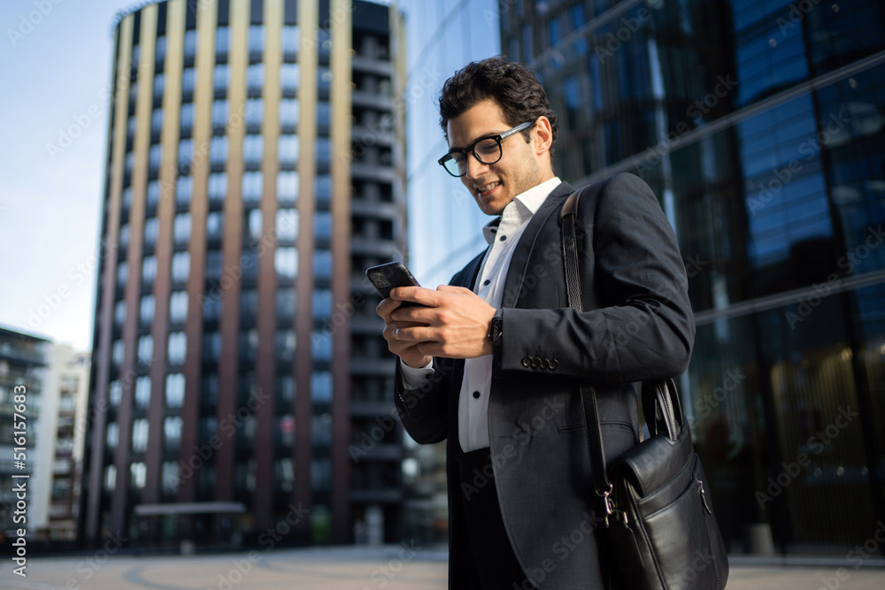 A man with glasses writes a text message to a client on the phone, goes to work in the office in a business suit A man with glasses writes a text message to a client on the phone, goes to work in the office in a business suit