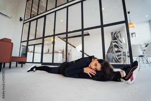 Young female wearing black sports suit exercising yoga pose indoors.