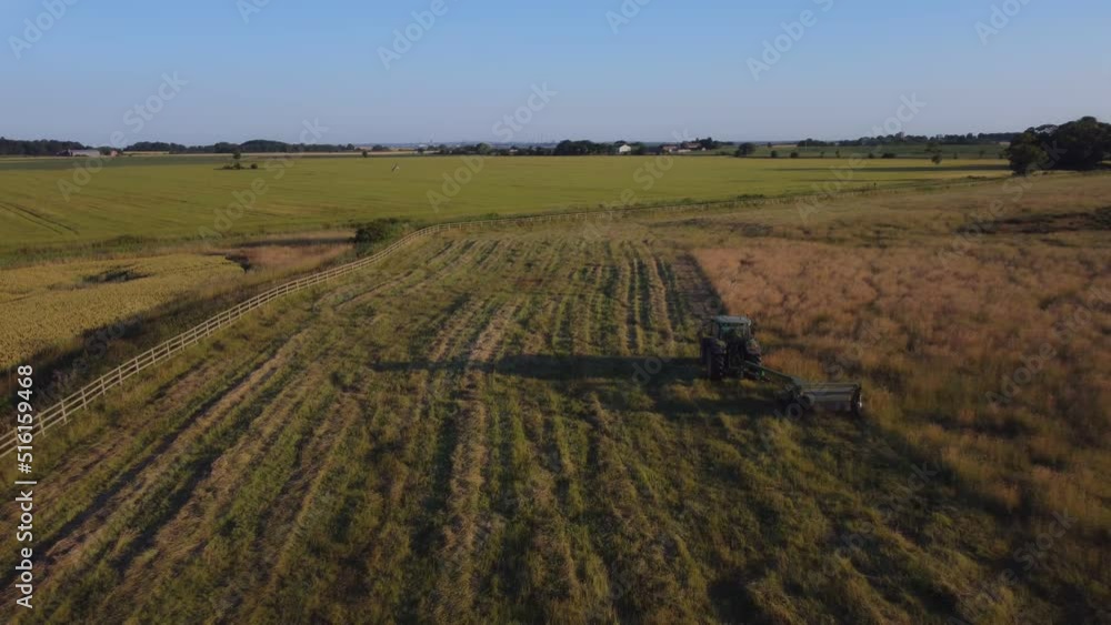 A green tractor cutting grass in field opposite a corn, wheat field. The sun is setting. Filmed with DJI Mavic mini 2. East Yorkshire. UK. A green tractor cutting grass in field opposite a corn, wheat field. The sun is setting. Filmed with DJI Mavic mini 2. East Yorkshire. UK.