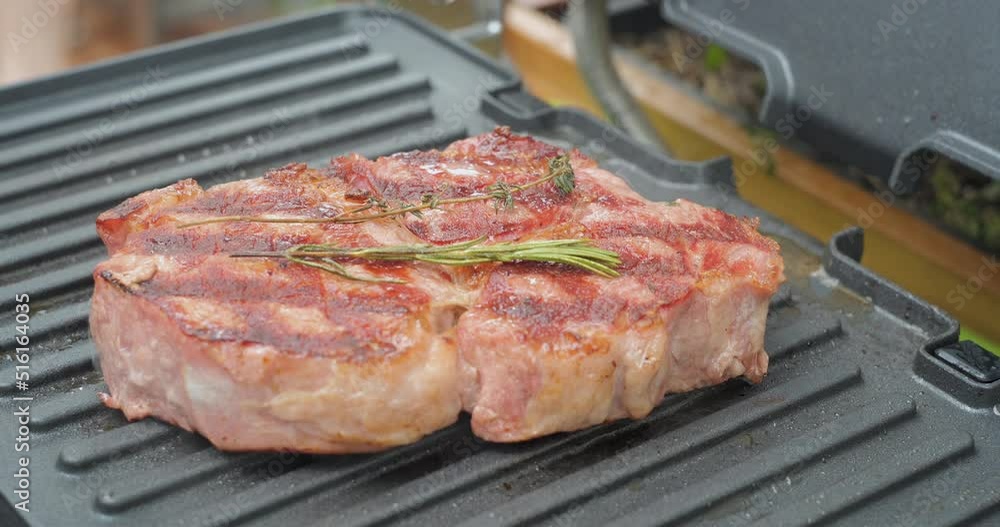 Juicy beef steak with rosemary is cooked on an electric grill Juicy beef steak with rosemary is cooked on an electric grill