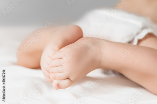 The baby crawls on a white bed. Legs of a newborn look straight