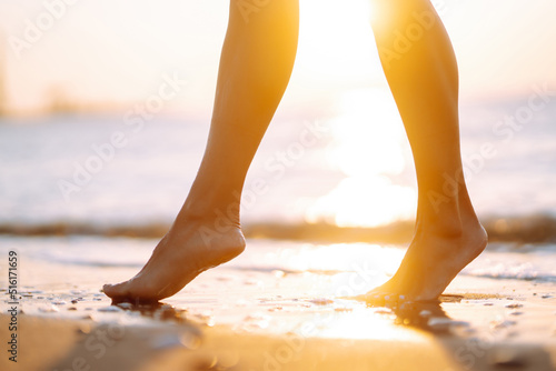Close- up leg of young woman walking along wave of sea water and sand on the summer beach. The concept of relax, travel, freedom and summer vacation.