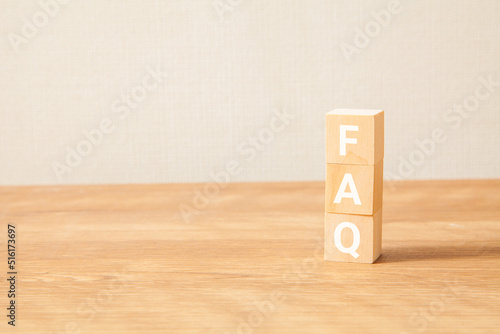 FAQの文字。よくある質問。Frequently Asked Questions。3つの木製ブロックに書かれている。白い文字。木製テーブルと白い壁紙の背景。左にコピースペース。