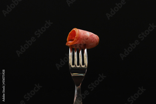 A slice of sausage on a fork on a black background. Close-up