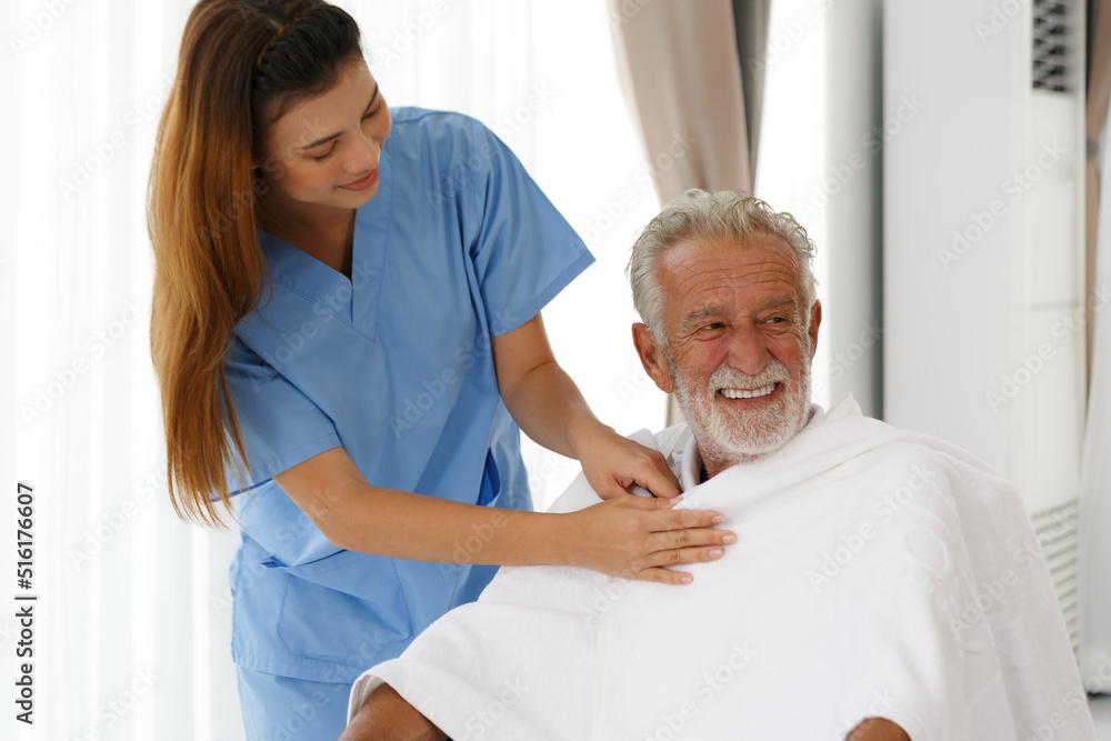 Obraz premium A female nurse uses a blanket to a senior Caucasian man sitting in a wheelchair