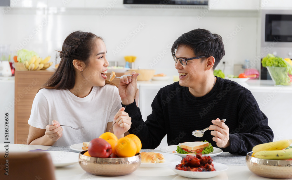 young Asian couple Happy to sit and eat at the dining table in the kitchen at home