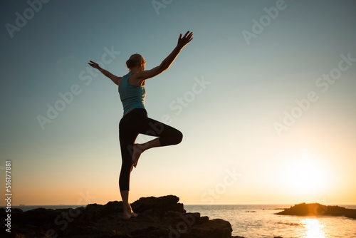 A woman performs yoga exercises on the sea beach during sunset.