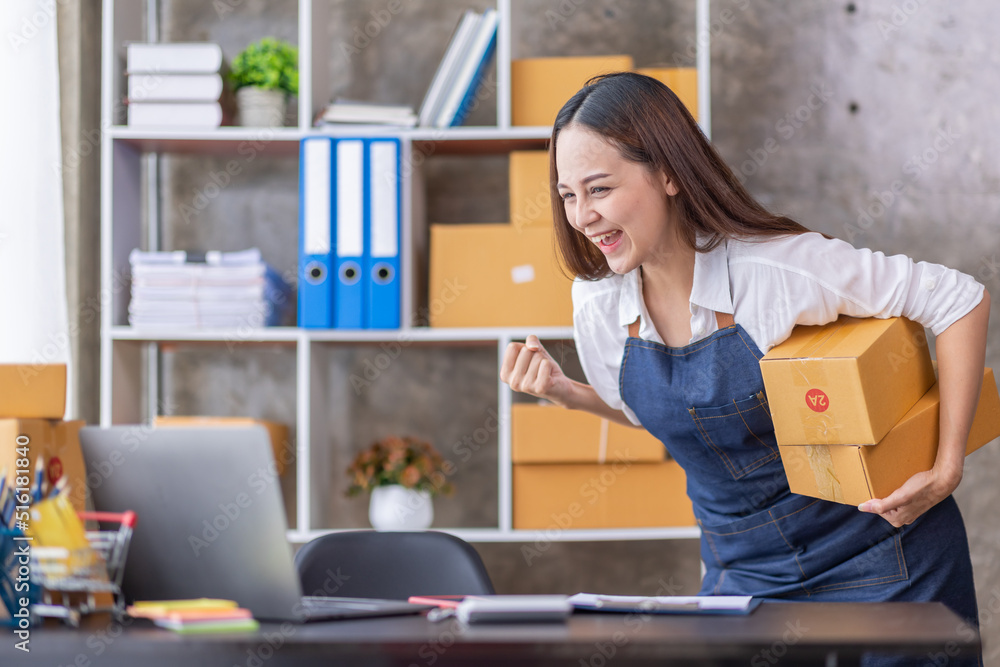 Startup SME small business entrepreneur of freelance Asian woman using a laptop with box Cheerful success happy Asian woman her hand lifts up online marketing packaging and delivery SME idea concept Startup SME small business entrepreneur of freelance Asian woman using a laptop with box Cheerful success happy Asian woman her hand lifts up online marketing packaging and delivery SME idea concept