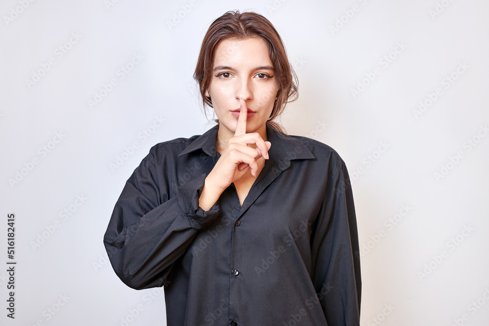 A beautiful girl shows a gesture with a finger near her lips, thereby indicating to be quiet.