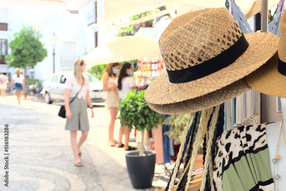 Straw hat with black stripe hanging outside of a local store in a touristic town by the Mediterranean sea in summer. Tourists coming to street market. High quality photo