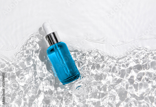 Blue cosmetic bottle on the water surface. Blank label for branding mock-up. Summer water pool fresh concept. Flat lay, top view.