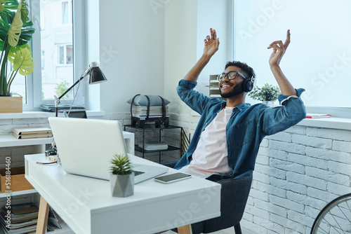 Relaxed African man in headphones gesturing while sitting at working place