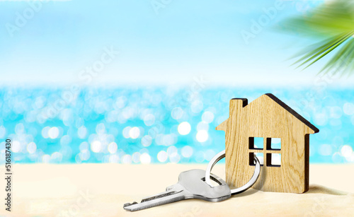 House by the sea concept. Figure of house and key on sandy beach