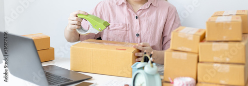 Woman in a pink shirt is packing in the mailbox to prepare to deliver it to the customer, New business style for young people working at home and owning businesses, Sell online or online sell concept. © Puwasit Inyavileart