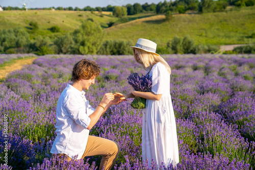 couple in white outfit in lavender field, photo session. man is proposing to woman with ring. engagement day. romance and true love in relationship