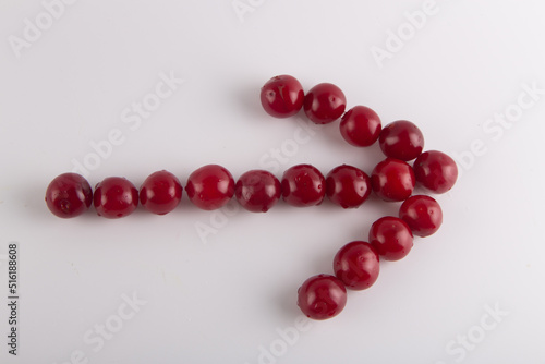 Cherry arrow on white background. Top view on fresh wet red fruits lay in shape of pointer to right.