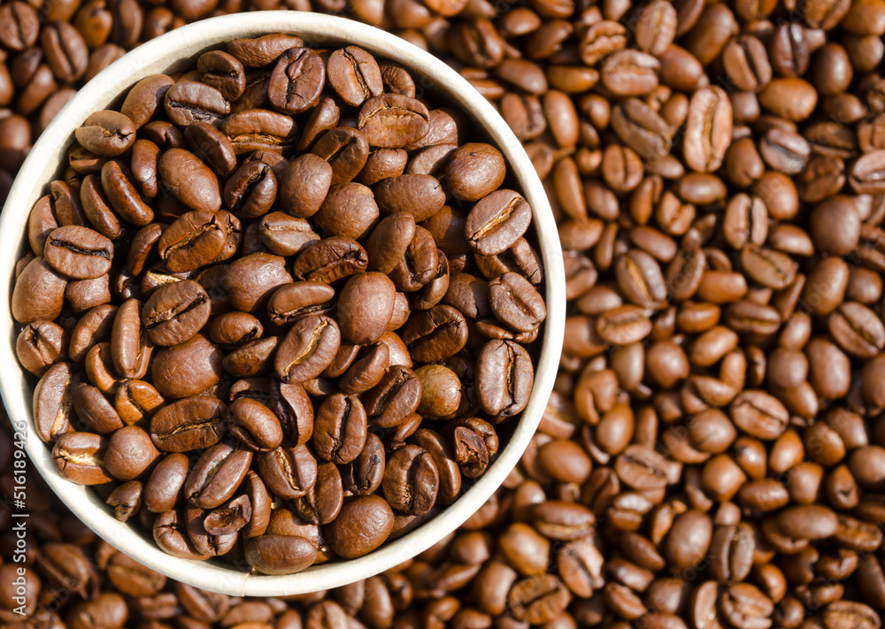Roasted coffee beans in a paper cup against the background of not sharp coffee beans. Roasted coffee beans in a paper cup against the background of not sharp coffee beans.
