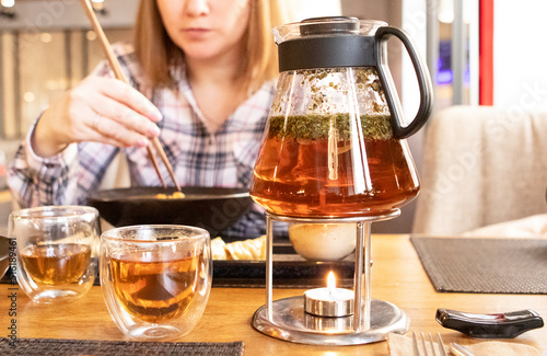 a girl eats japanese food with chopsticks in a restaurant. teapot with tea on the table