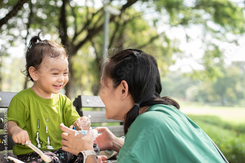 Asian parent in public garden, happy baby girl with green t shirt eating yogurt lookat her mom, smiling