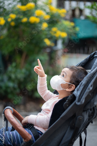 Asian baby wear surgical face mask sitting on stroller looking up and point finger up, COVID