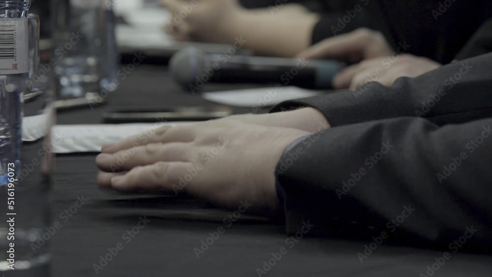 Group of business people sitting in a line at conference. Close-up of participants of press conference sitting at the table in a row in front of audience. Close up microphone