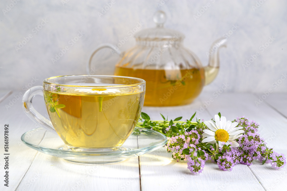 Herbal tea with chamomile and thyme in a transparent cup on a white wooden table Herbal tea with chamomile and thyme in a transparent cup on a white wooden table