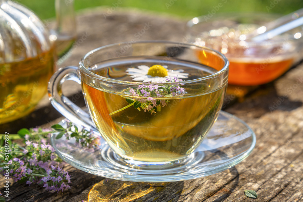 Herbal tea with chamomile and thyme in a transparent cup on an old wooden table on a sunny day Herbal tea with chamomile and thyme in a transparent cup on an old wooden table on a sunny day