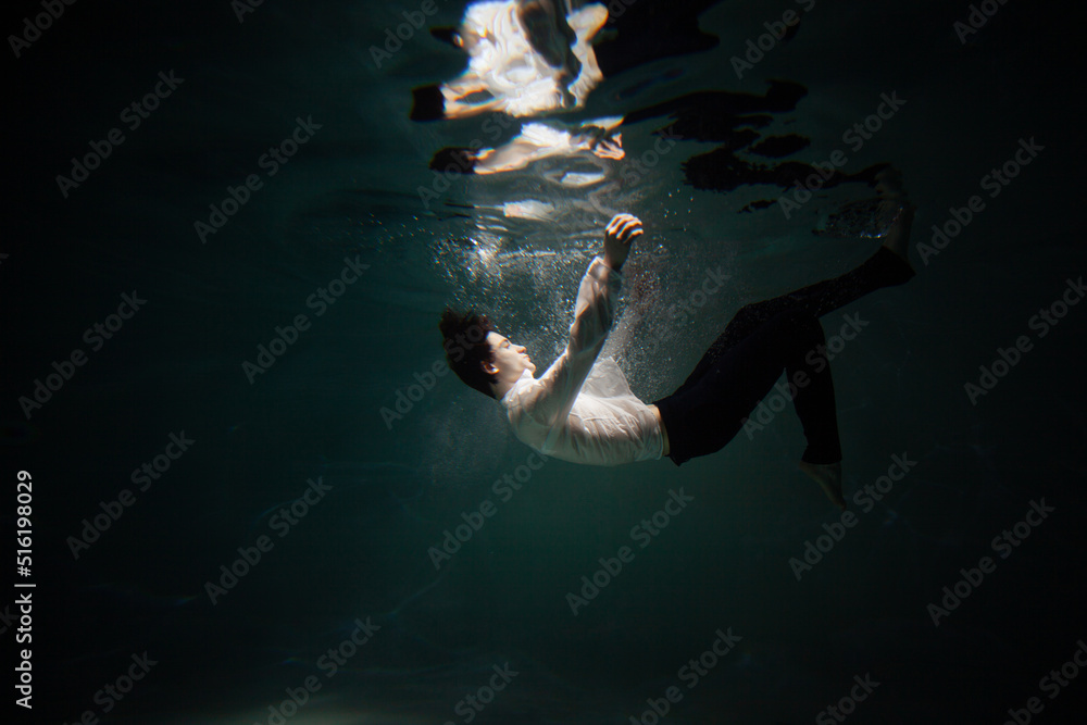 Sink. A young man is going to the bottom. A guy in a white shirt and trousers falls under the water, calmness and acceptance of fate - obrazy, fototapety, plakaty 