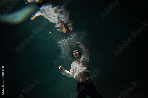 underwater shooting with contrasting light, a guy in a white shirt and pants screaming underwater, panicking and afraid of drowning, falling into the water, a crime.