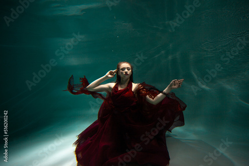 Beautiful underwater shooting, a young woman in a red dress with a long skirt swimming underwater, distortion and caustic effects.