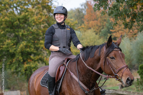 junge Frau lacht bei Ausritt auf braunem Pferd im Herbst © mavcon