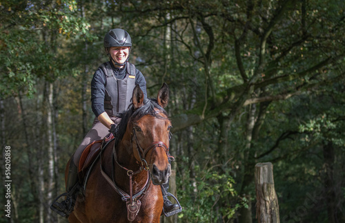 junge Frau lacht bei Ausritt auf braunem Pferd im Wald © mavcon