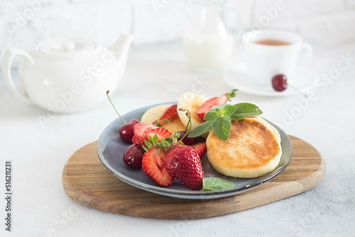 Cottage cheesecakes with berries and mint in a grey plate on a white background teapot and cup of tea.