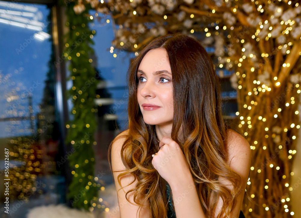 A beautiful brunette girl in a green dress in a New Year's modern interior. Lights and bokeh effect. Christmas. Beauty and fashion concept. Copy space on the left A beautiful brunette girl in a green dress in a New Year's modern interior. Lights and bokeh effect. Christmas. Beauty and fashion concept. Copy space on the left