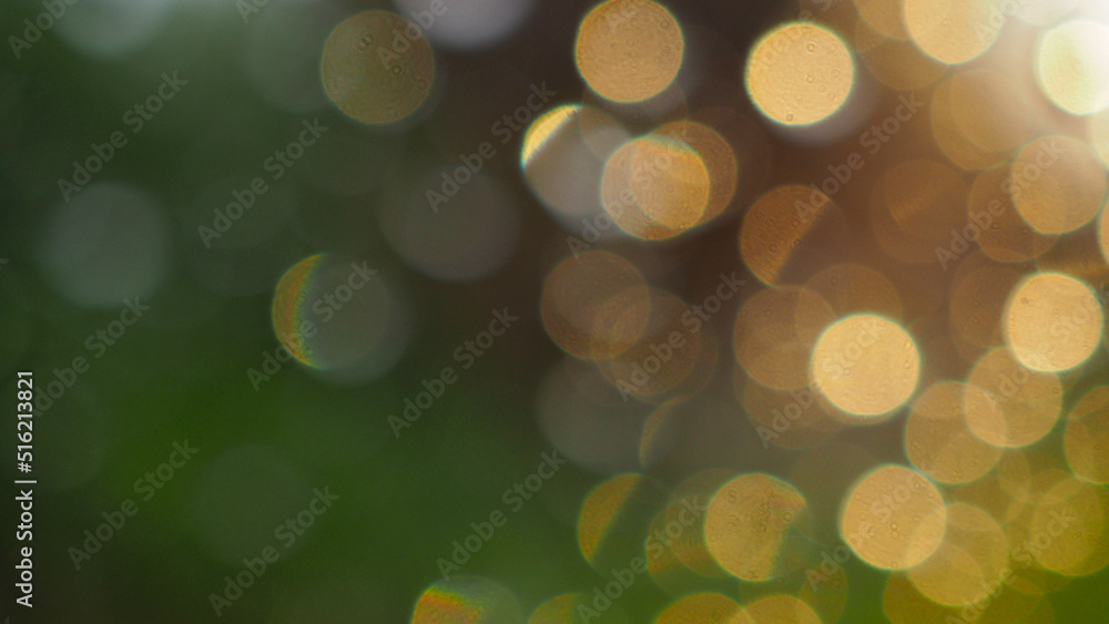 Fototapeta premium Abstract background. Blurred raindrops on a window glass at sunset. Yellow round spots on a green backdrop. Natural bokeh wallpaper. Macro