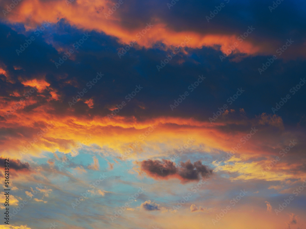 Cloudy sky at sunset. Dark blue and yellow natural background or wallpaper. The rays of the setting sun effectively illuminate the clouds. Beautiful and spectacular evening skies. Nightfall cloudscape
