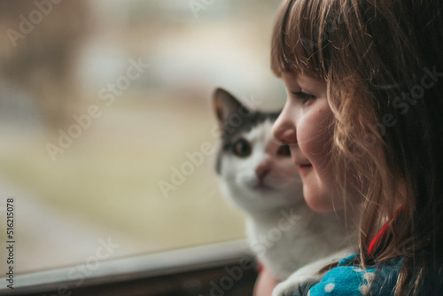 little girl with a cat in her arms look out the window  rainy day  home comfort