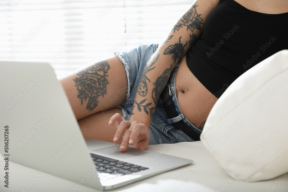 Naklejka premium Beautiful woman with tattoos on body using laptop in living room, closeup