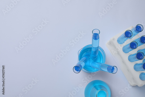Laboratory glassware with blue liquid on light grey background, flat lay. Space for text