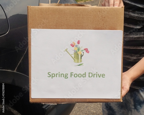 Arms Holding Cardboard Box with Spirng Food Drive Sign in Front of Black photo