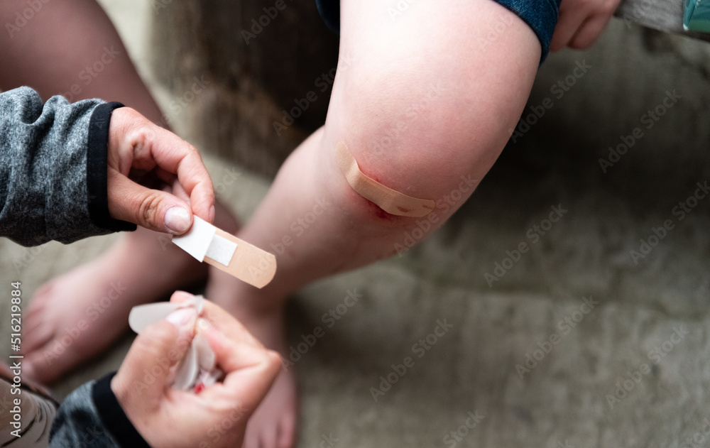 Baby's bruised knee. A mother putting a plaster on her son's injured knee. Dressing with a plaster on the boy's leg.