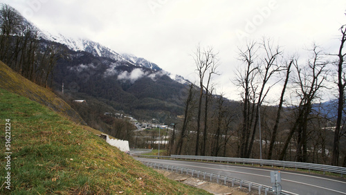 Breathtaking landscape of a mountain road and a moving car on cloudy background with snowy mountain. Stock footage. Mountain serpentine road with driving vehicle.