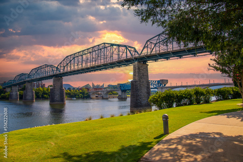 the majestic Walnut Street Bridge over the rippling blue waters of the Tennessee River surrounded by lush green trees and buildings with powerful clouds at sunset at Coolidge park in Chattanooga photo