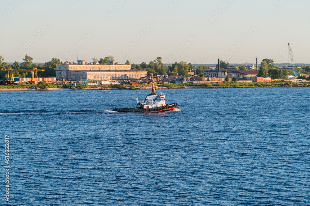 a tugboat sails along the wide river Severnaya Dvina northern part of Russia against the background of industrial structures on the shore